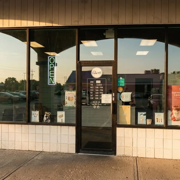 Exterior of a Zellan WIT bubble tea shop with an "OPEN" neon sign and menu posters in the windows.