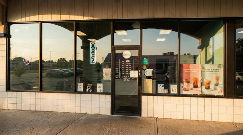 Exterior of a Zellan WIT bubble tea shop with an "OPEN" neon sign and menu posters in the windows.