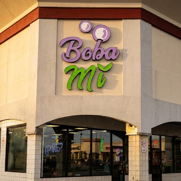 Exterior of Boba Mi restaurant with purple and green signage, under a cloudy sky.