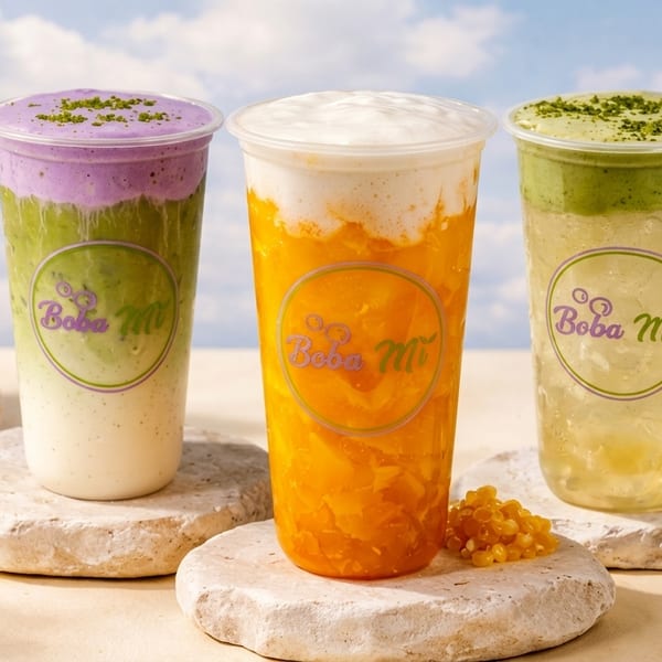 Three colorful Boba Mi drinks on stone coasters with a blue sky background and daisies.