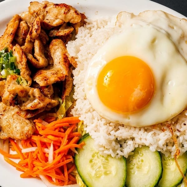 Grilled chicken, white rice, fried egg, pickled carrots, and cucumber slices on a white plate.