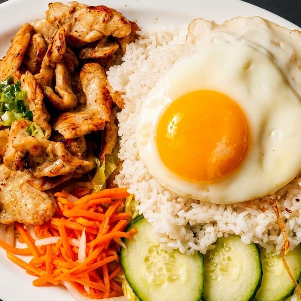 Grilled chicken, white rice, fried egg, pickled carrots, and cucumber slices on a white plate.